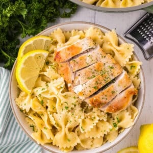 overhead view of a serving of lemon chicken pasta with parmesan and lemon wedges in a bowl.