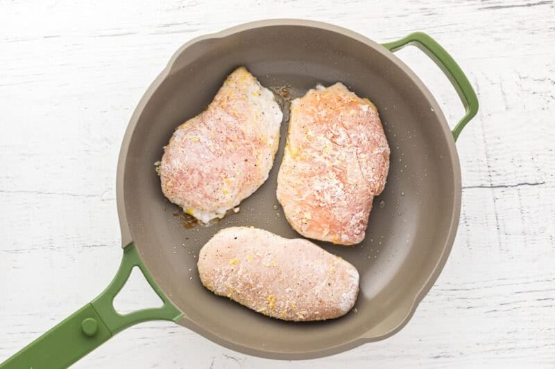 floured chicken breasts searing in a pan.