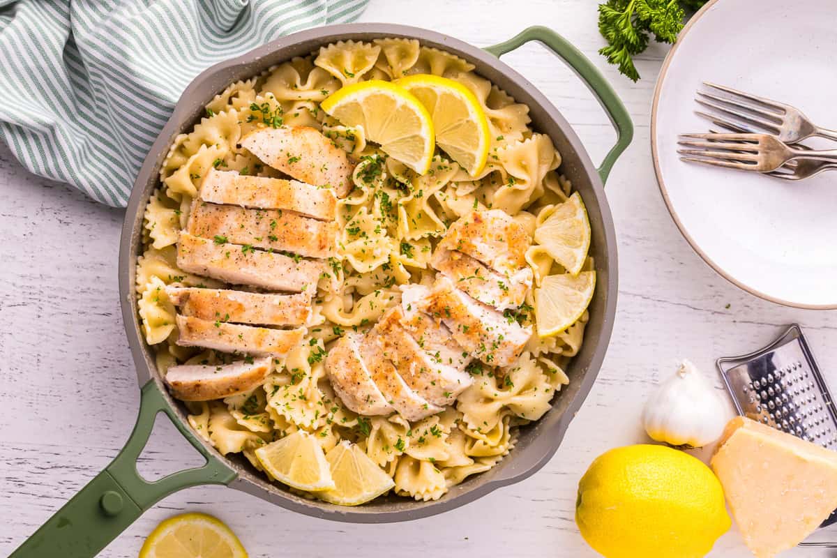 overhead view of lemon chicken breasts and pasta in a pan with lemon wedges and parsley.