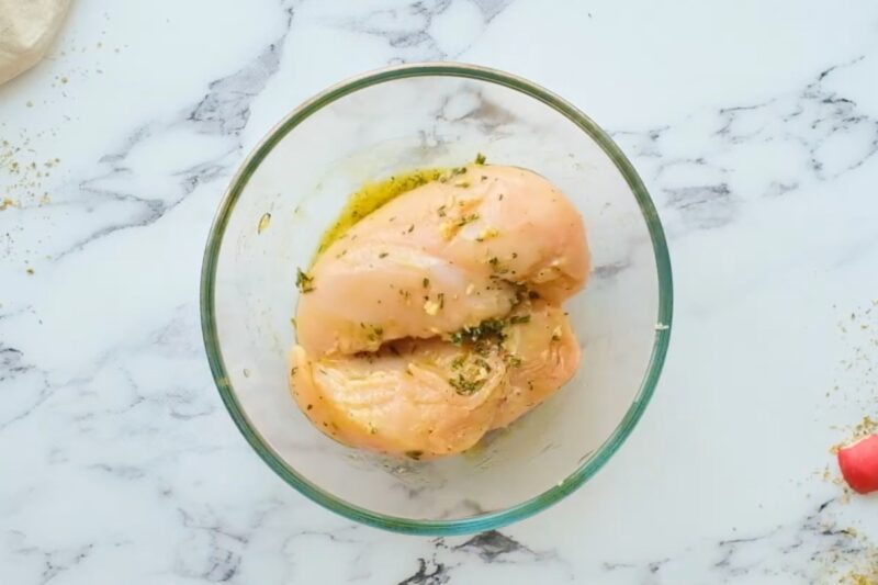 Chicken breasts marinating in a bowl.