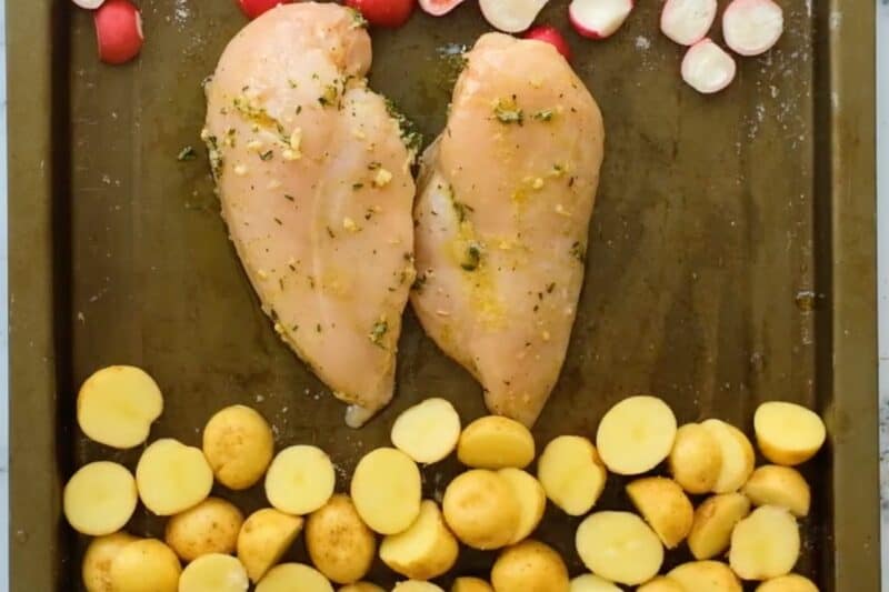 Marinated chicken breast and potatoes on a sheet pan, before baking.