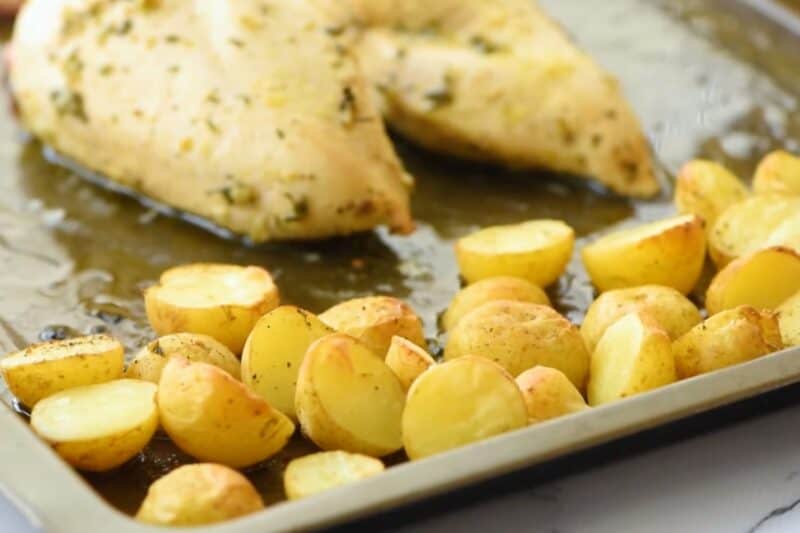 Chicken breasts and potatoes on a sheet pan.