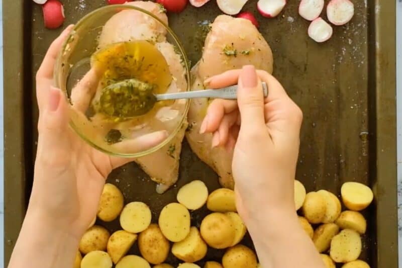 Pouring marinade over chicken and potatoes on a sheet pan.
