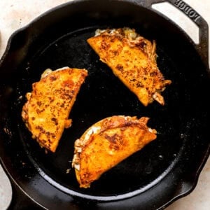 3 crispy, cheesy chicken birria tacos in a cast iron skillet.