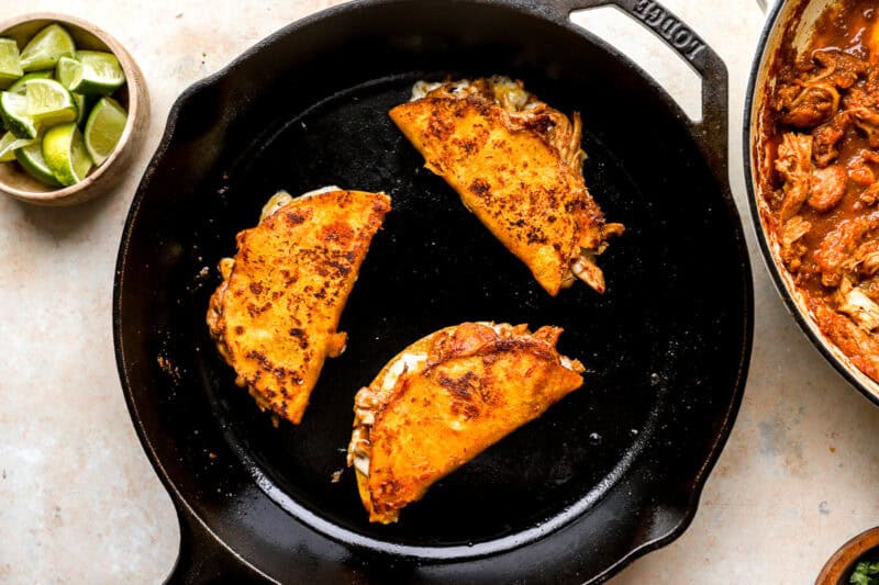 3 crispy, cheesy chicken birria tacos in a cast iron skillet.