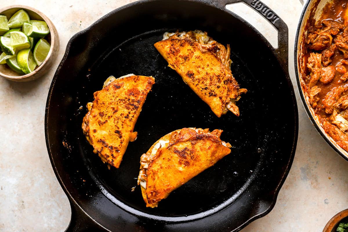 3 crispy, cheesy chicken birria tacos in a cast iron skillet.