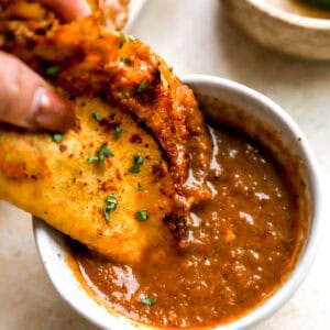 dipping a chicken birria taco into birria consommé.