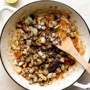 seasoned onions and chili peppers in a pan with a wooden spoon.