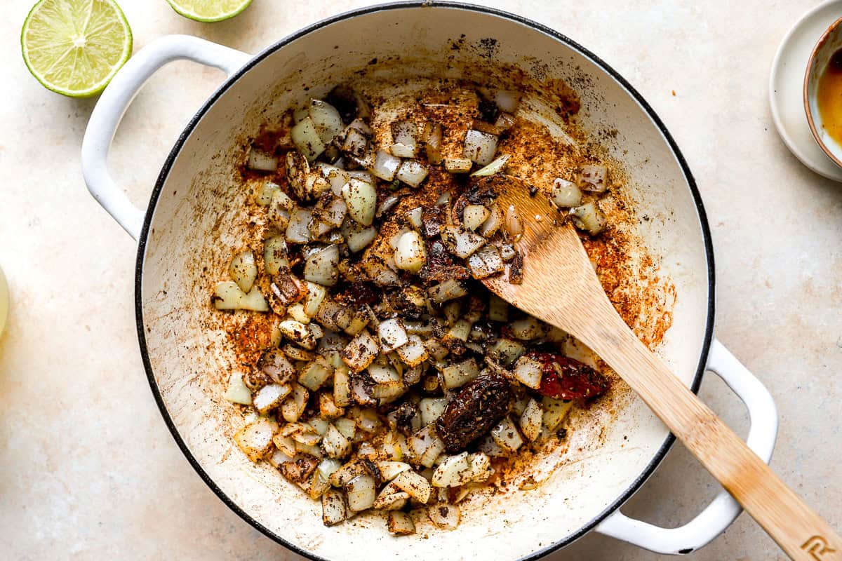 seasoned onions and chili peppers in a pan with a wooden spoon.