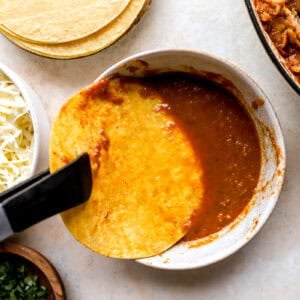 dipping a corn tortilla in birria sauce with tongs.