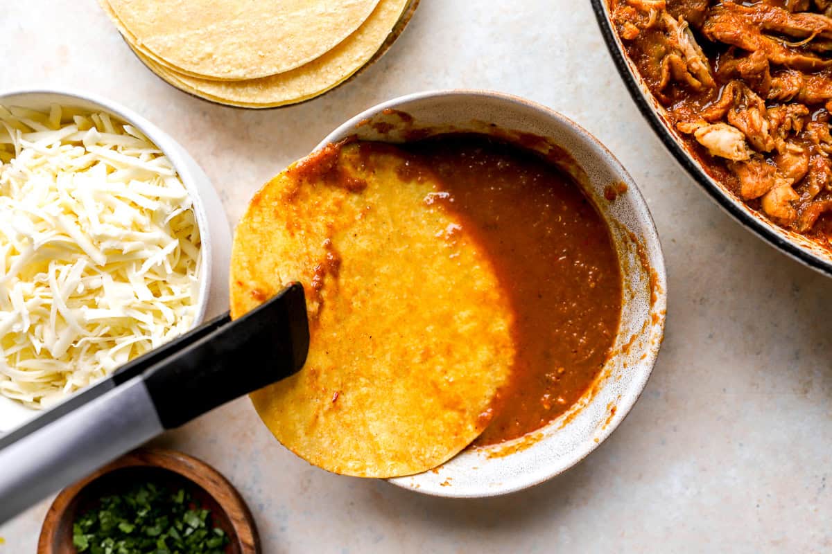 dipping a corn tortilla in birria sauce with tongs.