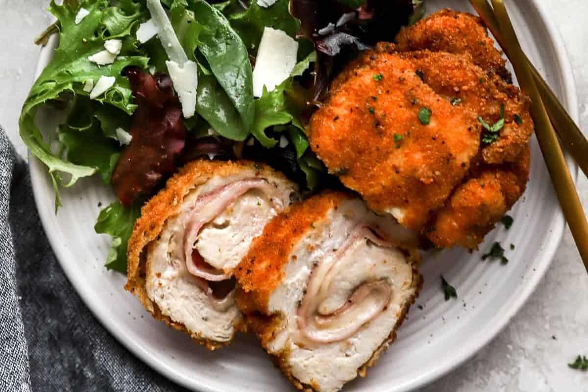 a sliced serving of chicken cordon bleu on a white plate with salad greens.