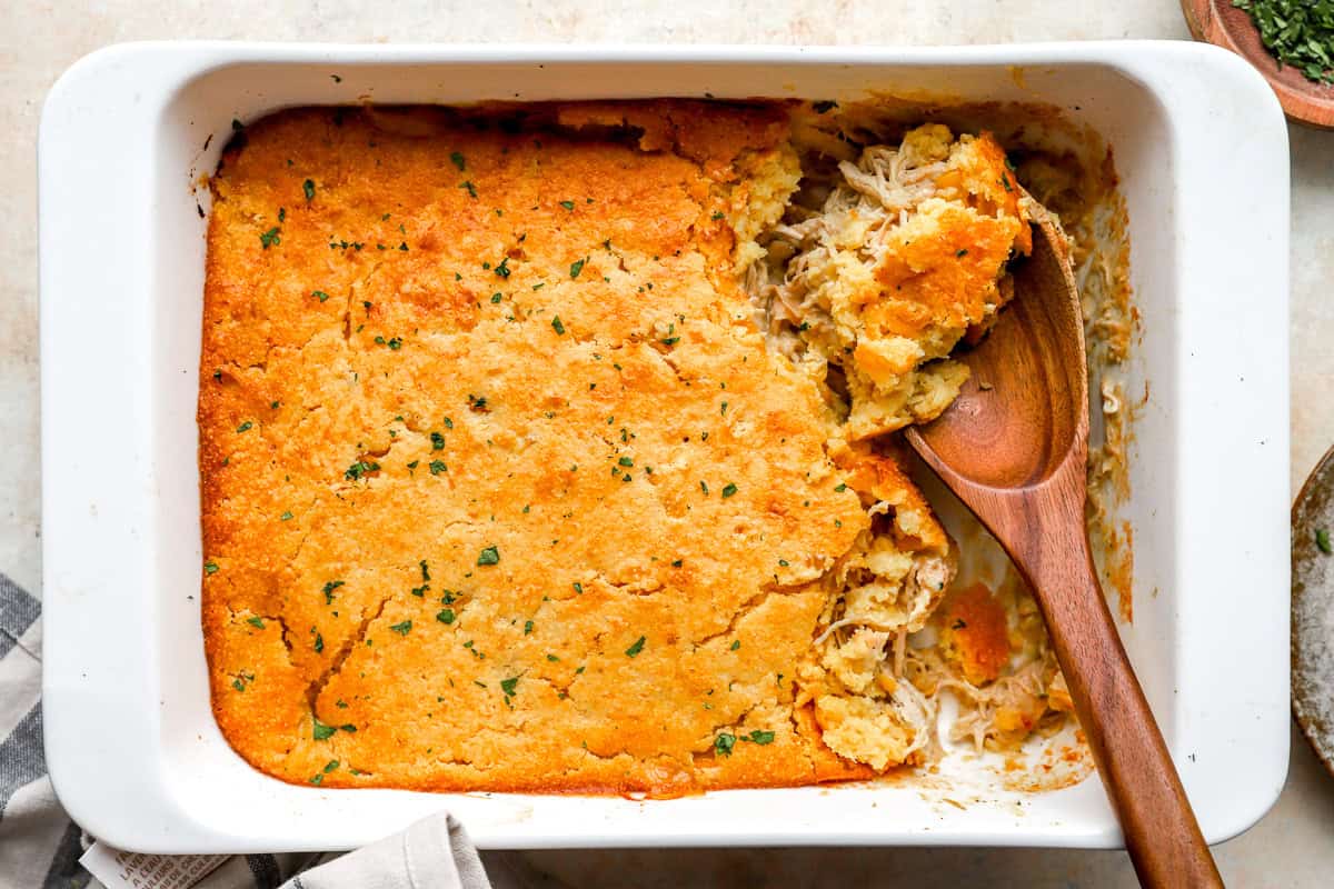 partially eaten chicken cornbread mix casserole in a casserole dish with a wooden spoon.