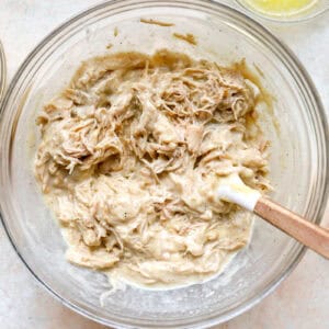 shredded chicken casserole mixture in a glass bowl with a rubber spatula.
