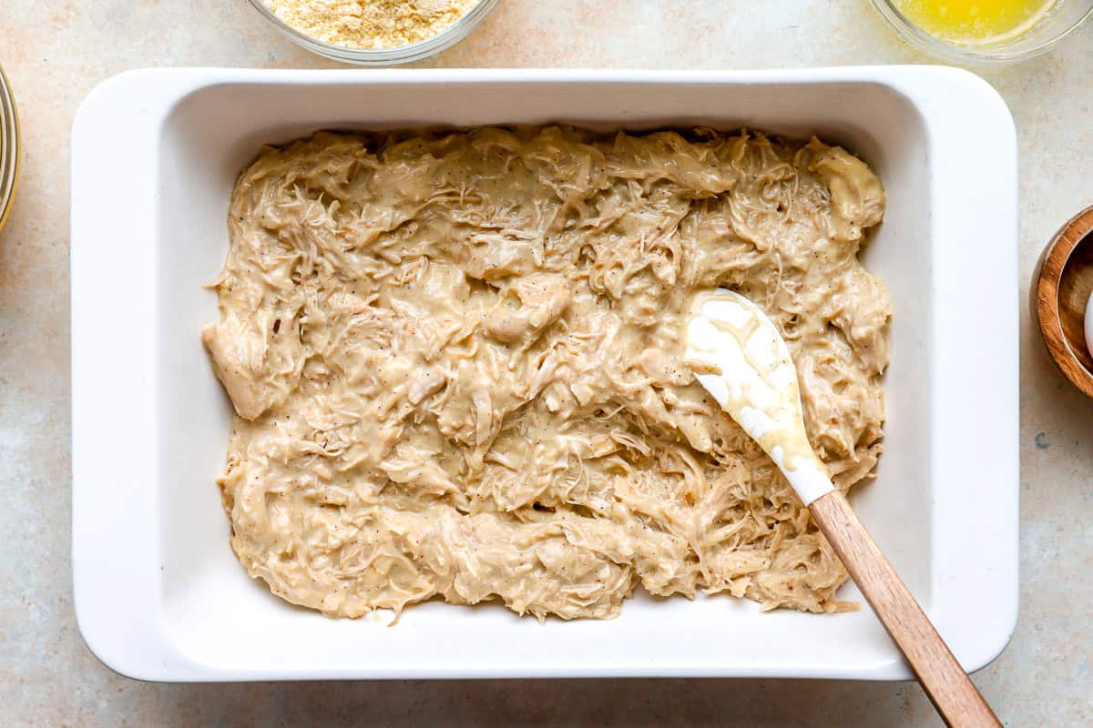 shredded chicken casserole mixture in a casserole dish with a rubber spatula.