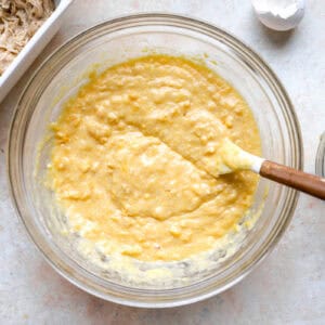 cornbread batter in a glass bowl with a rubber spatula.