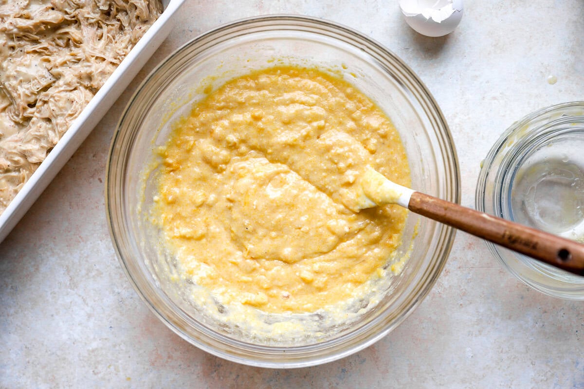 cornbread batter in a glass bowl with a rubber spatula.