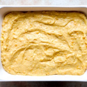 cornbread batter spread over shredded chicken casserole in a casserole dish.