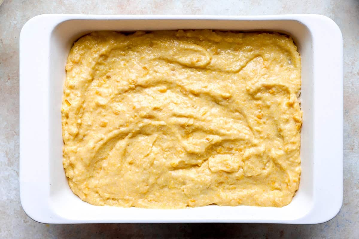 cornbread batter spread over shredded chicken casserole in a casserole dish.