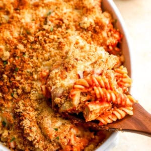 lifting a scoop of chicken parmesan casserole from a casserole dish with a wooden spoon.