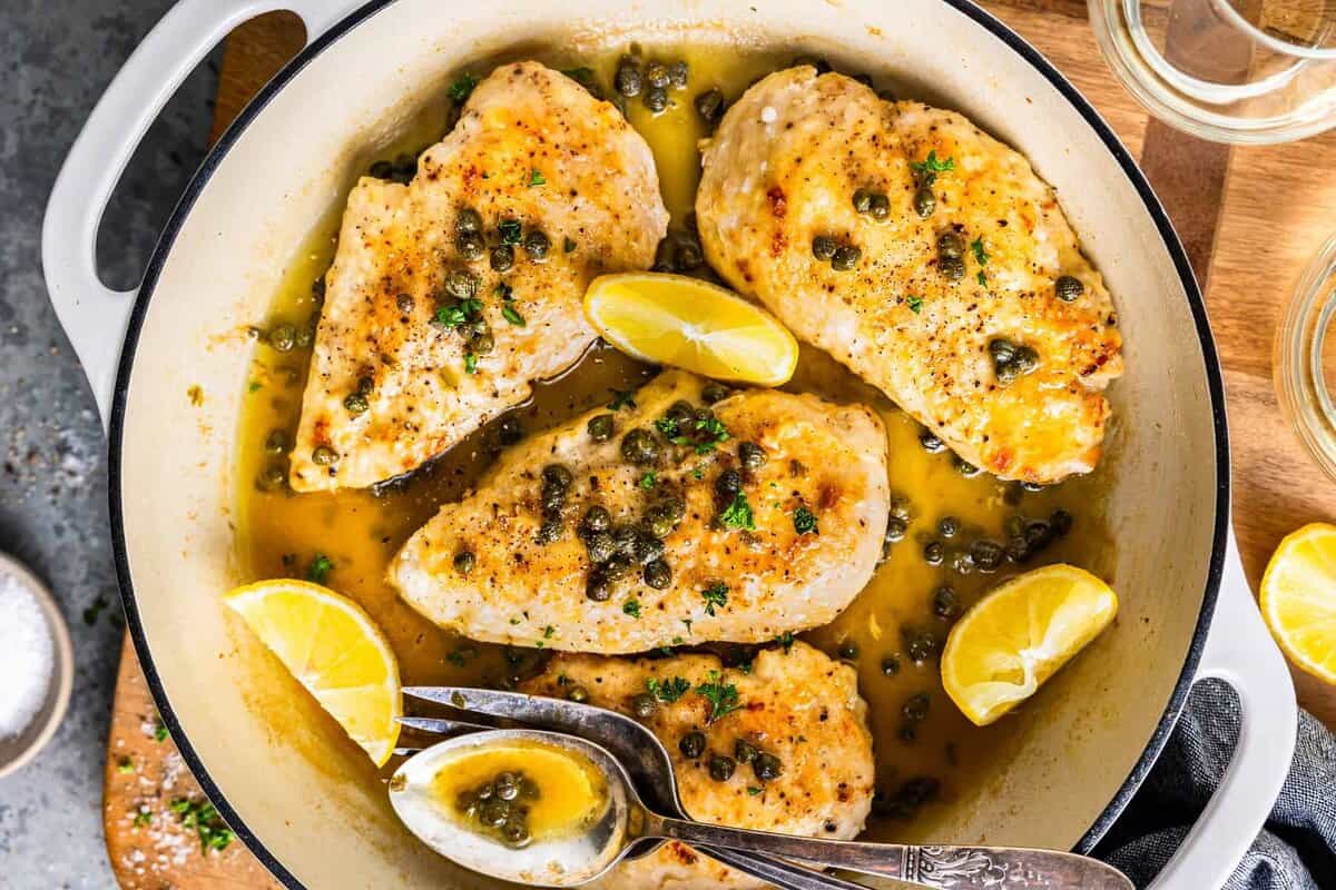chicken piccata with lemon and spoon in white skillet