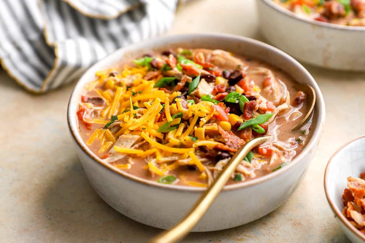 a bowl of crack chicken chili topped with bacon, cheese, and scallions.