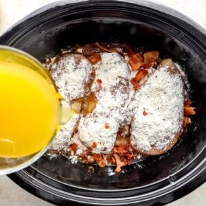 pouring chicken broth over seasoned chicken breasts and veggies in a crockpot.