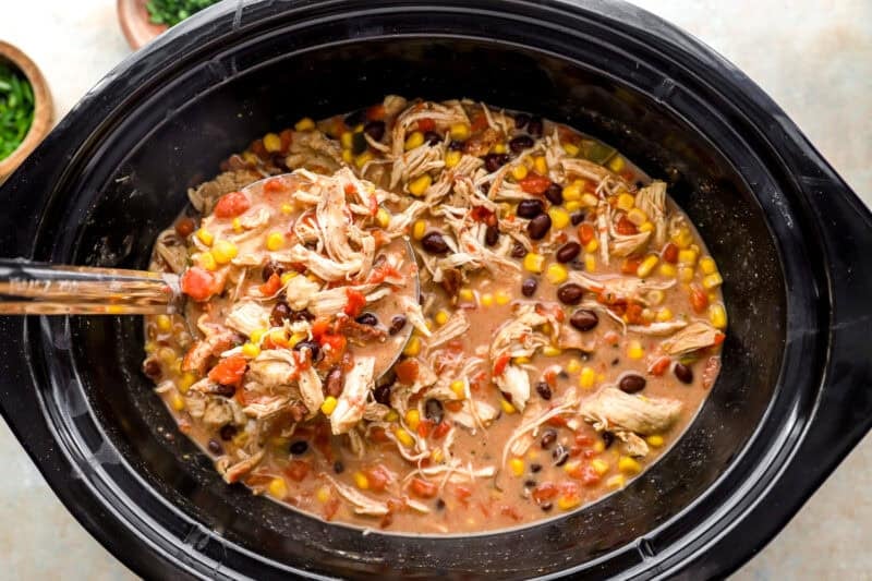 crack chicken chili in a crockpot with a ladle.