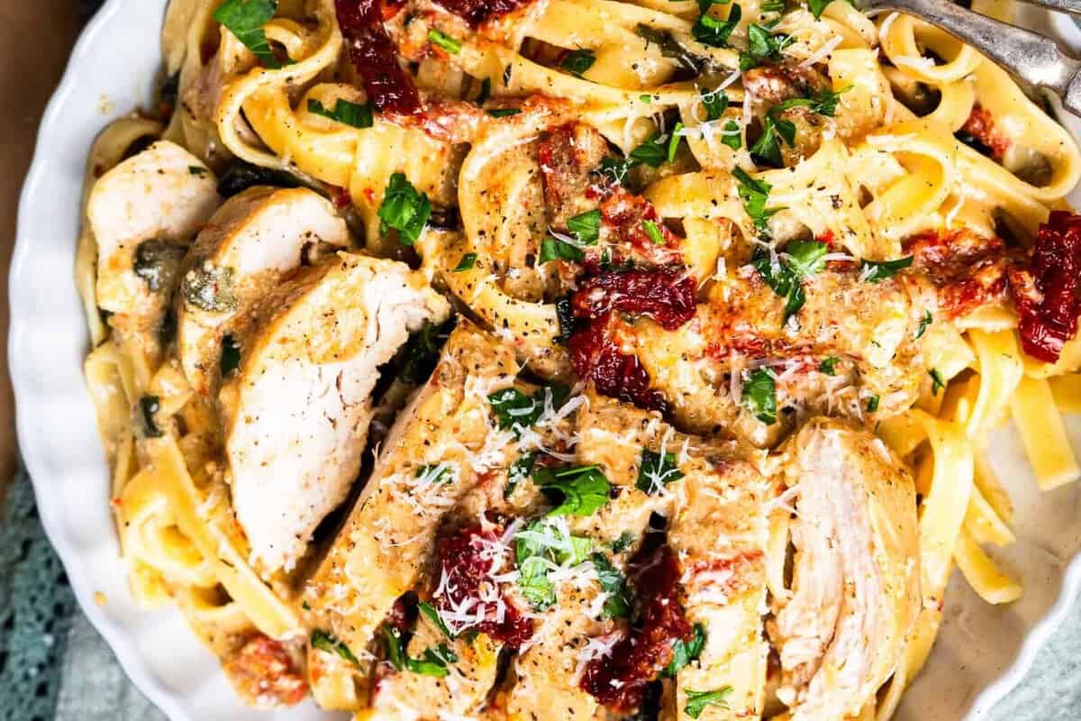 a sliced serving of tuscan chicken on a white plate with pasta.