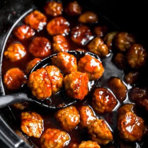 scooping grape jelly chicken meatballs from a crockpot.