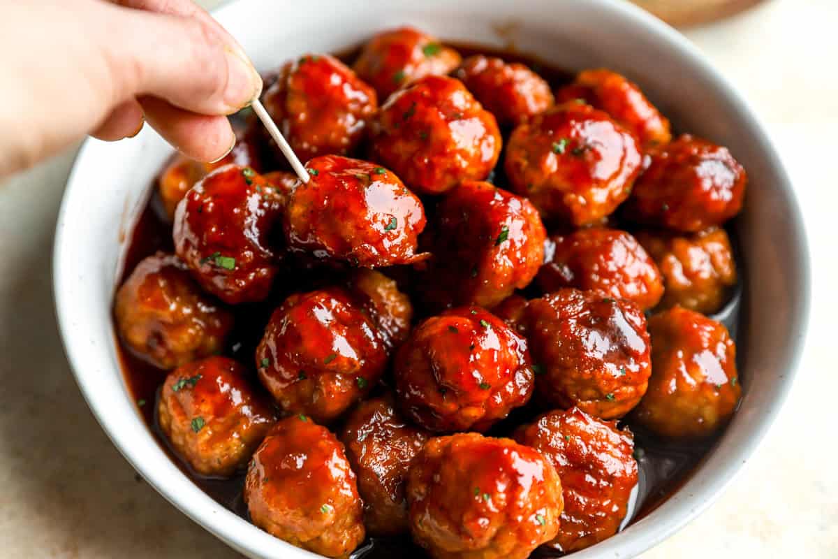 poking a grape jelly cocktail meatball with a toothpick.