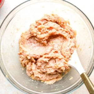 chicken meatball mixture in a glass bowl with a rubber spatula.