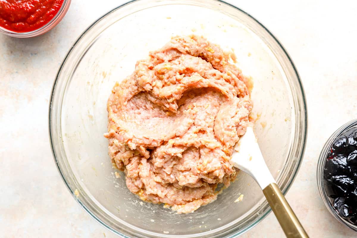 chicken meatball mixture in a glass bowl with a rubber spatula.