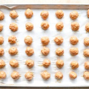 raw chicken meatballs on a lined baking sheet.