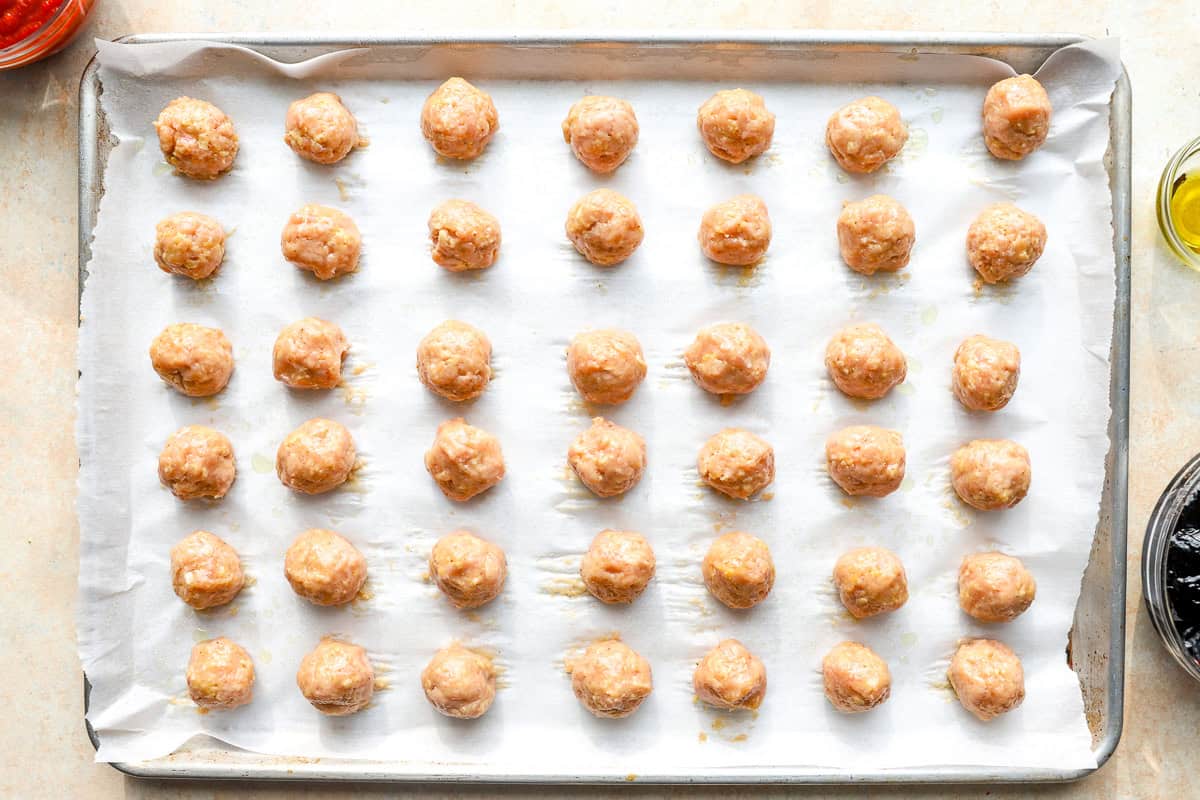 raw chicken meatballs on a lined baking sheet.