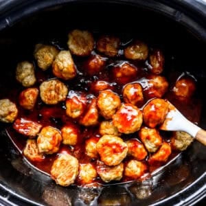 tossing chicken meatballs in grape jelly and chili sauce in a slow cooker with a rubber spatula.