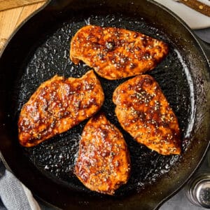 seared chicken breasts topped with hoisin glaze and sesame seeds in a cast iron pan.