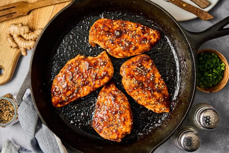 seared chicken breasts topped with hoisin glaze and sesame seeds in a cast iron pan.