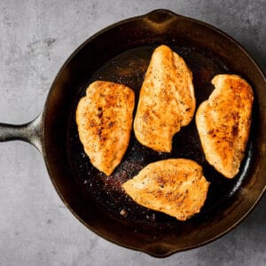 four seasoned seared chicken breasts in a cast iron pan.