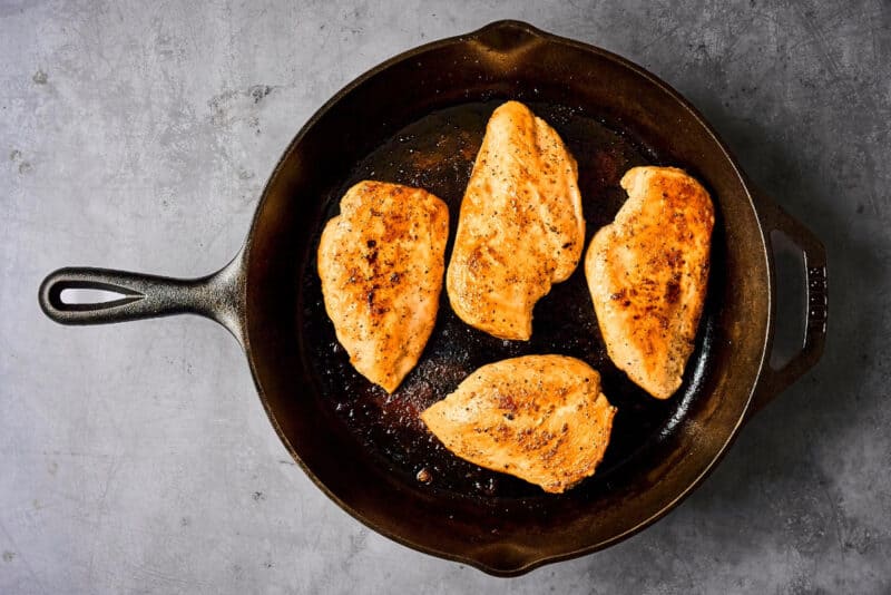 four seasoned seared chicken breasts in a cast iron pan.