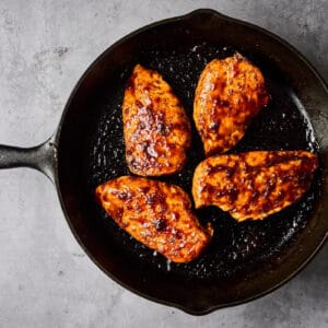 seared chicken breasts topped with hoisin glaze in a cast iron pan.