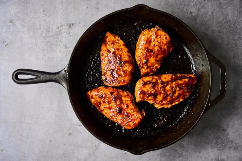 seared chicken breasts topped with hoisin glaze in a cast iron pan.