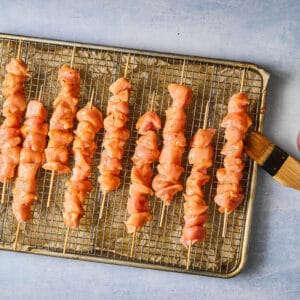 brushing raw chicken skewers with apricot marinade.