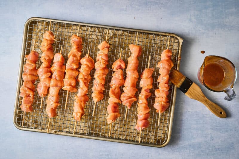 brushing raw chicken skewers with apricot marinade.