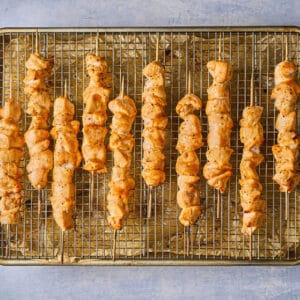 partially cooked apricot chicken skewers on a wire rack set in a baking sheet.