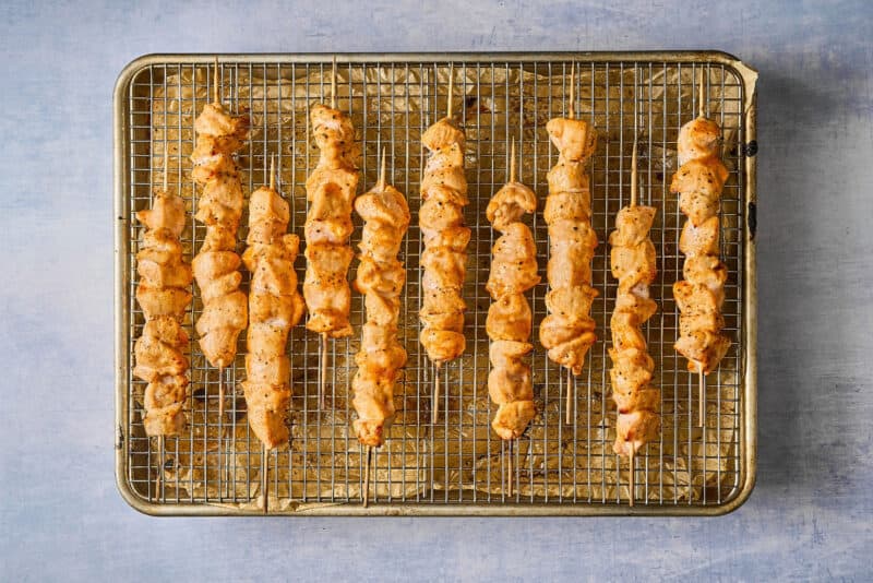 partially cooked apricot chicken skewers on a wire rack set in a baking sheet.