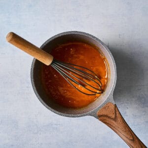 thickened apricot glaze in a saucepan with a whisk.