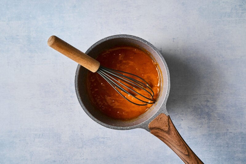 thickened apricot glaze in a saucepan with a whisk.