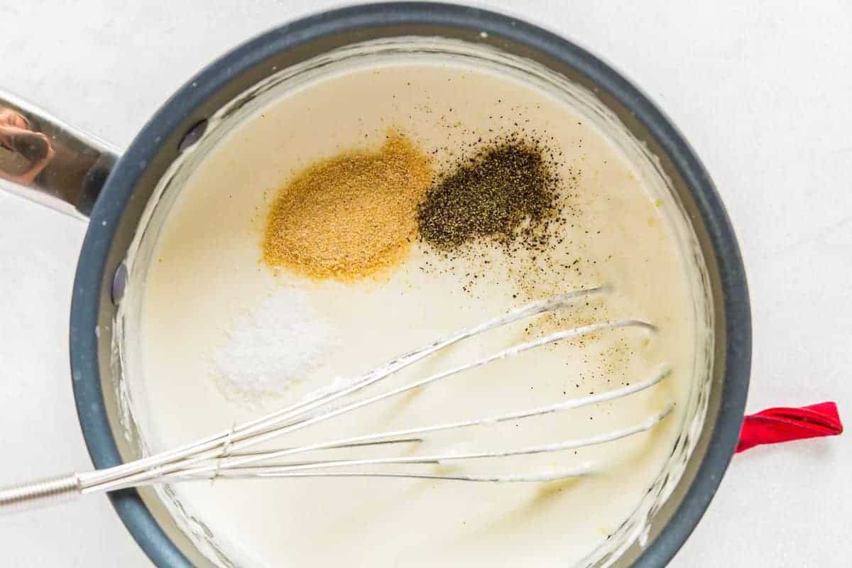 Adding spices to Alfredo sauce.