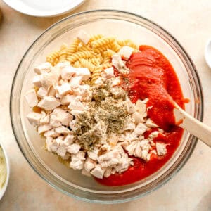 ingredients for chicken parmesan casserole in a bowl with a wooden spoon.